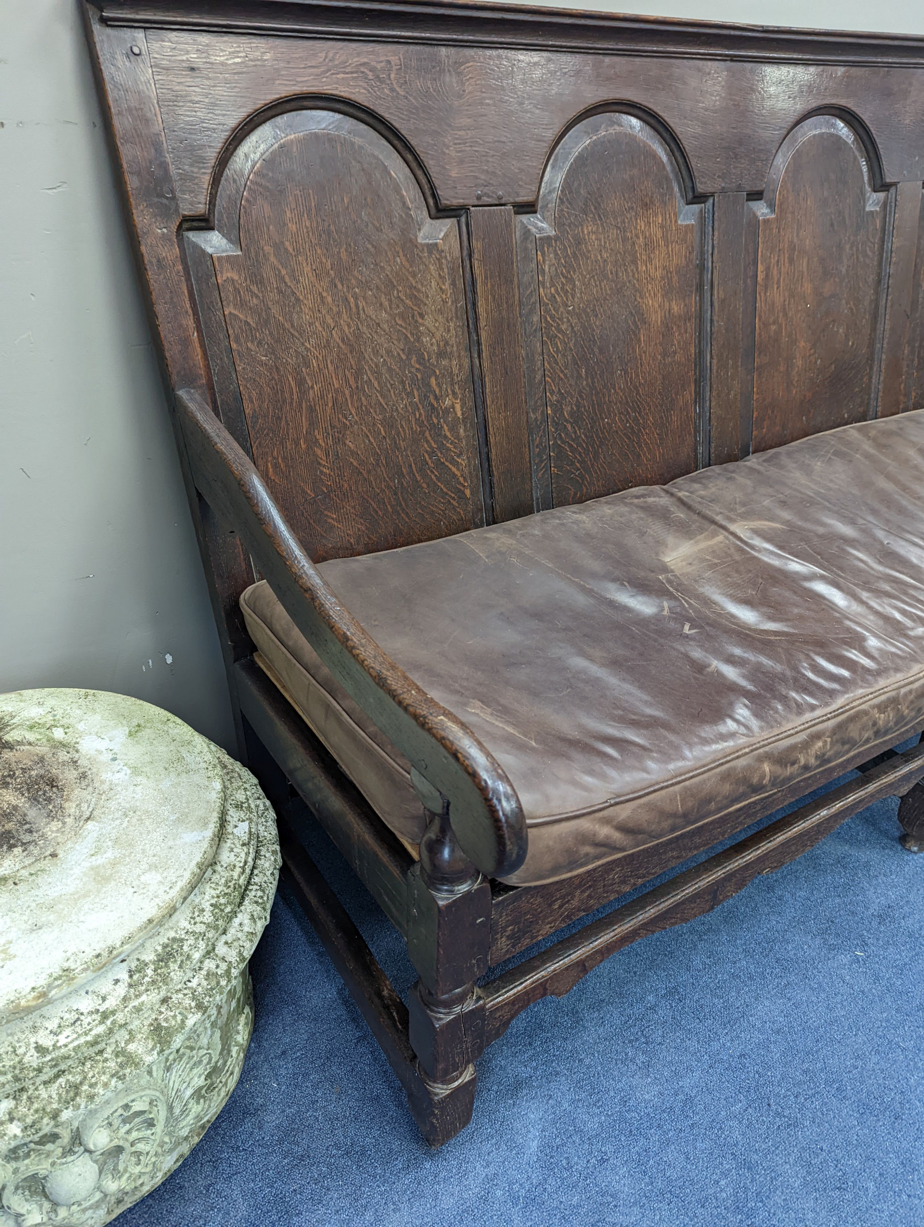 A mid 18th century panelled oak settle with leather squab seat, length 185cm, depth 77cm, height 114cm